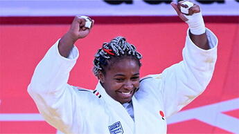 Portrait de Romane Dicko, judokate noire, sur le tatami, levant les bras en signe de victoire, alors qu'elle vient de remporter la médaille d'or aux championnats du monde 2022.