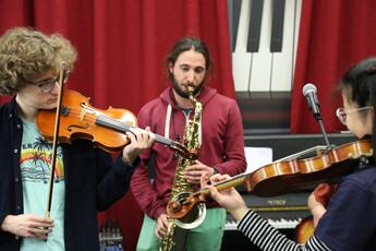 Trois étudiants joue de la musique, un joue du violn, un deuxième un saxophone, et une troisième (de dos) joue également du violon